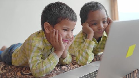 A shot of two Indian Asian preschool or primary male children or kids wearing uniforms is watching a funny video on a laptop and laughing together in an indoor setup. learning and education concept