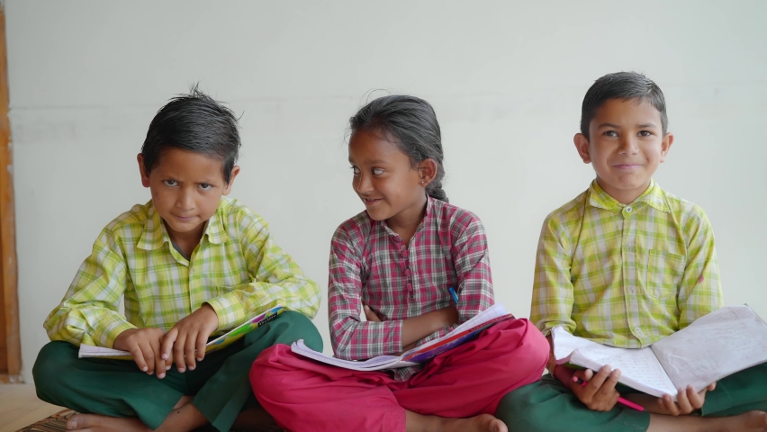 shot of trio Indian Asian primary school children wearing uniforms sitting together with text and note books looking happy against a white background or wall. learning and education concept Royalty-Free Stock Footage #1080914459