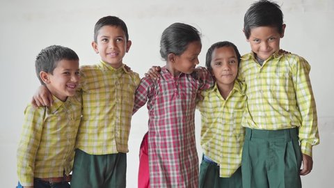 shot of a group of adorable primary school children wearing uniforms and backpacks with arms on each other shoulders looking happy against a white background or wall. learning and education concept