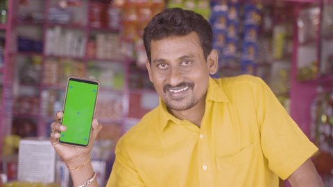 Smiling Merchant at groceries store hold mobile with green screen mock up by looking at camera - concept of Technology, advertisement, online booking and e-commerce