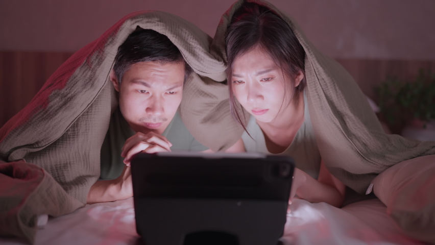 asian adult lover marry couple exited watching horror ghost online movie broadcast from laptop or tablet streaming on bed cover with blanket at home,home quarantine isolation lifetyle home interior