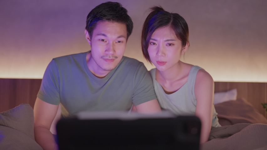 asian adult lover marry couple exited watching horror ghost online movie broadcast from laptop or tablet streaming on bed cover with blanket at home,home quarantine isolation lifetyle home interior