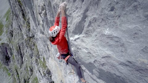 Alps, Switzerland, 12 July 2021: A woman rock climber climbs up a steep rock