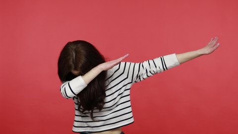 Woman dancing raising hands in dab dance pose, celebrating success, showing gesture of triumph, wearing casual style long sleeve shirt. Indoor studio shot isolated on red background.