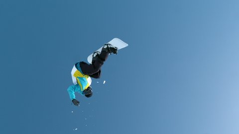 SLOW MOTION, TIME WARP: Snowboarder jumps off the kicker and does a rotating grab trick while riding in the Slovenian mountains on a sunny winter day. Spectacular shot of a man doing snowboard tricks.