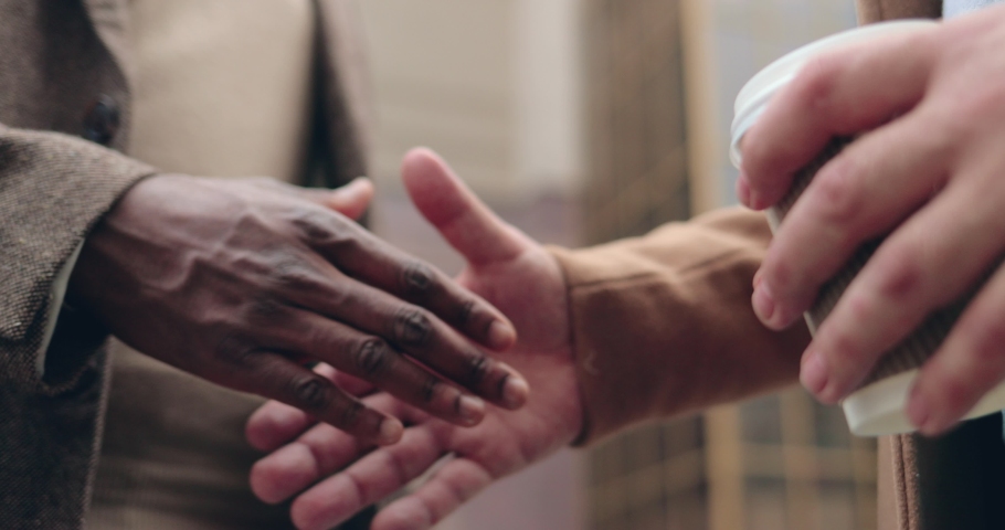 Close up of two men: African American and Caucasian businessmen made deal while shaking hands on the street.