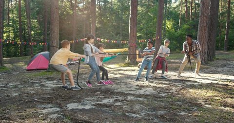 Full length view of the kids at summer camp playing tug of war with their multiracial teacher at the forest. Happy childhood and activities concept