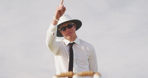 Caucasian male cricket umpire standing on a cricket pitch on a sunny day, making a signal to players on the pitch, pointing his finger in the air, with the wicket in the foreground, in slow motion