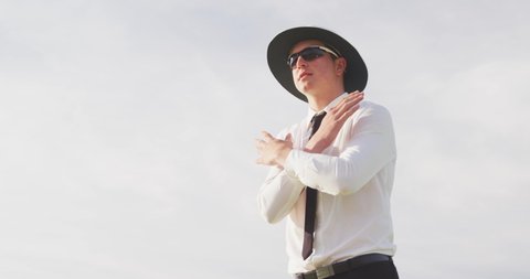 Caucasian male cricket umpire wearing white shirt and a wide brimmed hat, standing on a cricket pitch on a sunny day, signalling to players on the pitch, gesturing with his hands, in slow motion