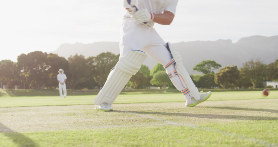 Teenage Caucasian male cricket player on the pitch wearing helmet, failing to hit the ball and getting bowled out during a cricket match with other players in the background, in slow motion Royalty-Free Stock Footage #1080921266