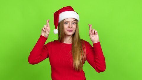 Teenager girl with christmas hat with fingers crossing and wishing the best. Making a wish over isolated background. Green screen chroma key