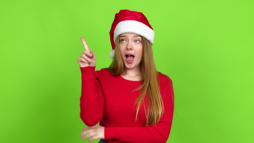 Teenager girl with christmas hat standing and thinking an idea pointing the finger up over isolated background
