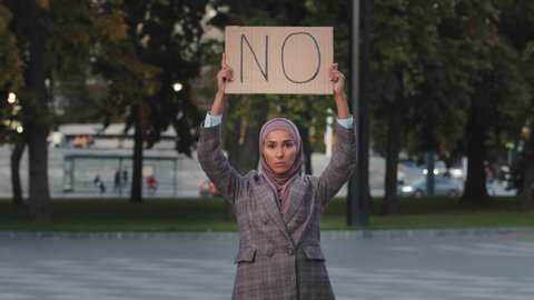Stop racism concept Arab immigrant Muslim woman in hijab protests against discrimination vax vaccination standing in city. Islamic girl holding cardboard slogan banner with text no disagree refusal