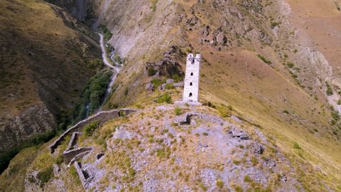 Mysterious aerial 4k drone footage – spin around lost ancient watchtower in Coj-Peda. High Caucasus mountains covered with yellow grass and mountain road on the background. Chechnya, Russia.