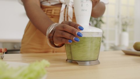 Midsection slowmo shot of unrecognizable African-American woman using blender while making healthy green smoothie at home