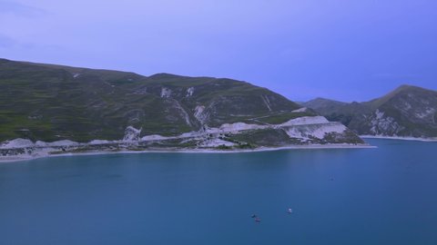 Beautiful aerial 4k drone nature footage – flying over the azure mountain lake Kezenoyam, towards one of the Caucasus mountains. Rowing boats with tourists are on the lake. Chechnya, Russia.