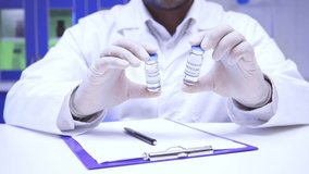 Cropped view of scientist holding jars with vaccines near clipboard in lab