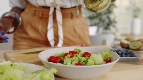 Midsection slowmo shot of unrecognizable African-American woman dressing fresh vegetable salad with olive oil