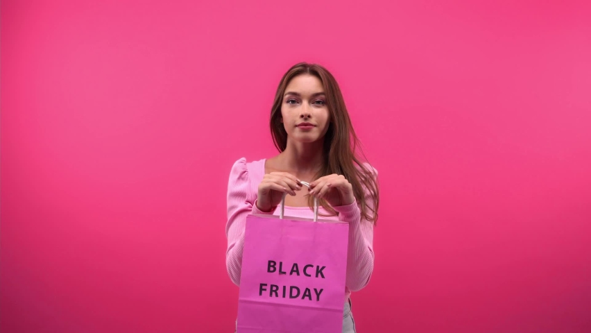 joyful woman holding shopping bag and perfume isolated on pink