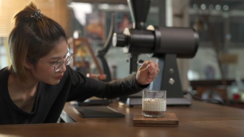 Asian woman barista make iced chocolate with froth milk in the glass on counter. Female coffee shop waitress employee prepare cold drink for customer at cafe. Small business coffee shop owner concept Arkivvideo