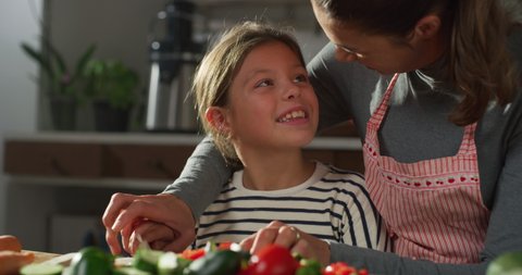 Cinematic authentic close up shot of happy mother teaching her little daughter how to cut with knife fresh vegetables for make healthy nutritious salad together for dinner in kitchen at home.