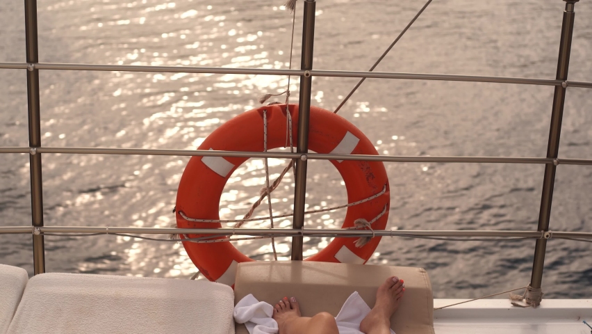 Two pedicured female legs and deck of sailing yacht during excursion along scenic sea landscapes. Woman sunbathing happily on deck of boat under open sunlight 