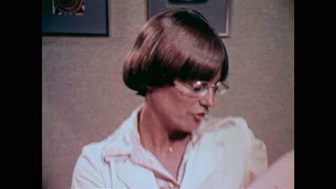 1980s: UNITED STATES: lady with glasses talks to patient in clinic. Patient nods head.