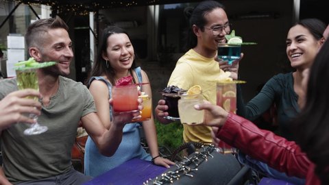 Diverse group of people enjoying party outdoors at cocktail bar - Happy trendy young friends celebrating together while cheering with elaborated cocktail in pub terrace