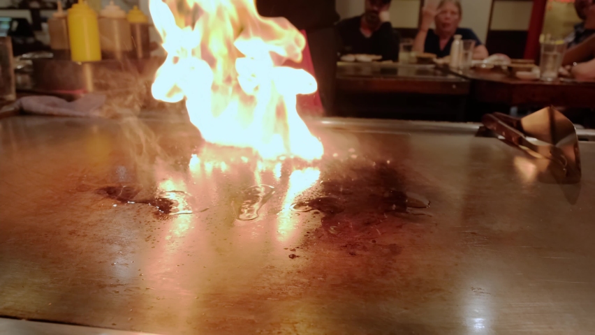Japanese chef cooking teppanyaki on hibachi. fire on hot plate. Slow motion