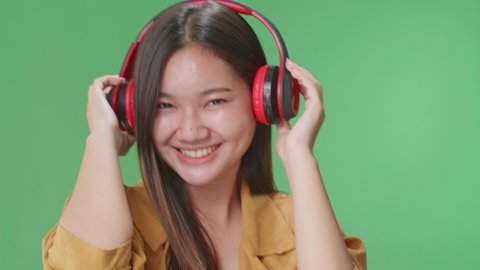 Close Up Of Asian Woman Listening To Music With Headphones And Dancing In The Green Screen Studio

