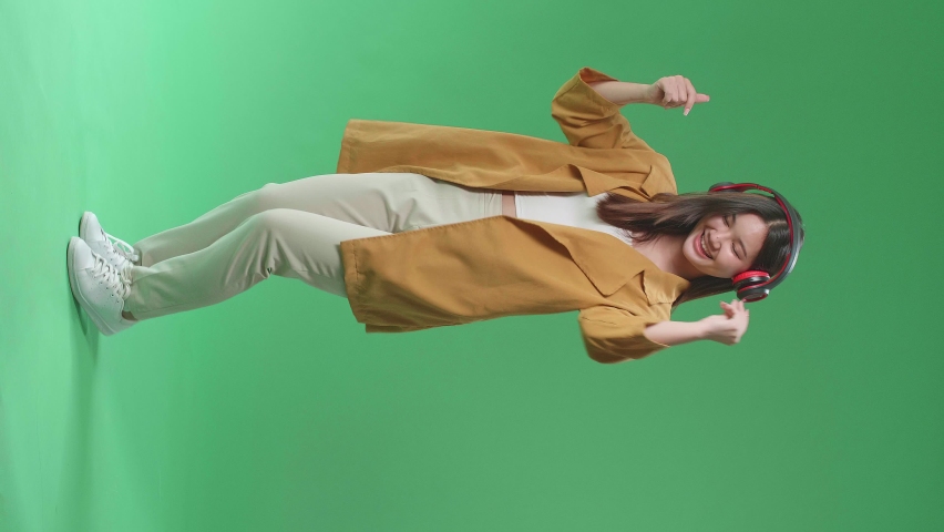 Full Body Of Asian Woman Listening To Music With Headphones And Dancing In The Green Screen Studio
