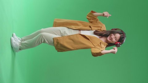 Full Body Of Asian Woman Listening To Music With Headphones And Dancing In The Green Screen Studio
