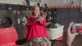 In laundry room hands hold phone shoots video on background blond woman listens to music dancing on camera. Housework service washing machine dryer indoors. Close up. Slow motion