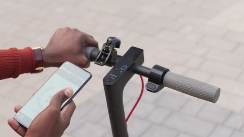 Slowmo close-up of unrecognizable African-American man activating electric scooter by app on his smartphone