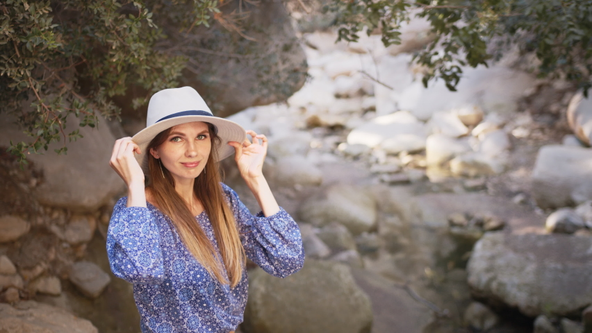 Portrait, Charming caucasian woman wearing summer hat and clothes walking among high rocks and looking around. Female tourist discovering new place during summer adventure. Charming woman in summer.