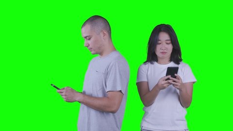 Young woman spying at mobile phone of her husband while standing in the studio. Shot in 4k resolution with green screen background