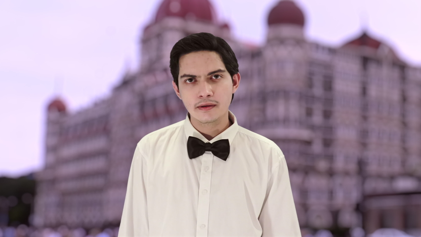 Handsome caucasian Indian boy holding his hands, with a beautiful dusk background of an ancient architecture building of Bombay. 4K ProRes