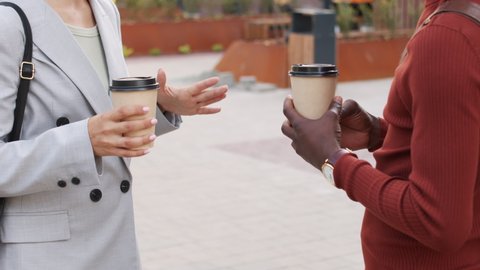 Midsection slowmo shot of hands of unrecognizable business partners holding paper coffee cups gesticulating during conversation outdoors