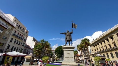 Huelva , Spain - 10 14 2021: Tilt down shot of walking tourist with face mask beside Christopher Columbus Statue in Huelva during sunny day