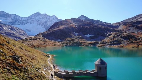 Aerial View Of Hikers Walking On The Trail With Intake Tower At Weisssee Reservoir In Austria.