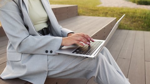 Slowmo midsection shot of hands of unrecognizable businesswoman wearing smart casual jacket and pants typing on laptop computer while working outdoors