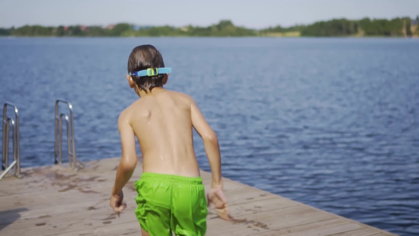 Little boy jumping into the lake from wooden pier. Having fun on summer day. Child diving in to the water.