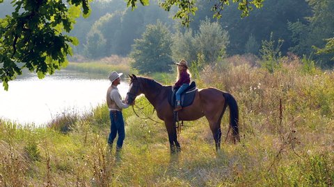 Cowboy and his daughter on horseback on the river bank. Happy cowboy family. Slow motion.
