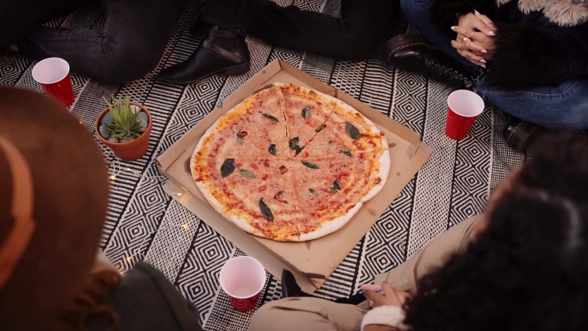 Multi-ethnic group of adult friends eating pizza out of pizza box at an outdoor party