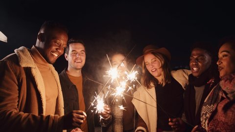 Multi-ethnic group of friends celebrating lighting their sparklers outdoors in the night time. High quality 4K footage 