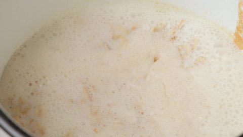 Add oat flakes to the boiling porridge. Close up. Healthy breakfast. 4k video