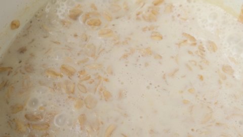 Cooking oatmeal porridge in saucepan and stir with wooden spoon. Close up. 4k video. Healthy breakfast