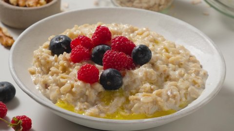 Adding nuts in oatmel porridge with butter and fresh berries in a plate. Healthy breakfast. Vegan food. 4k video