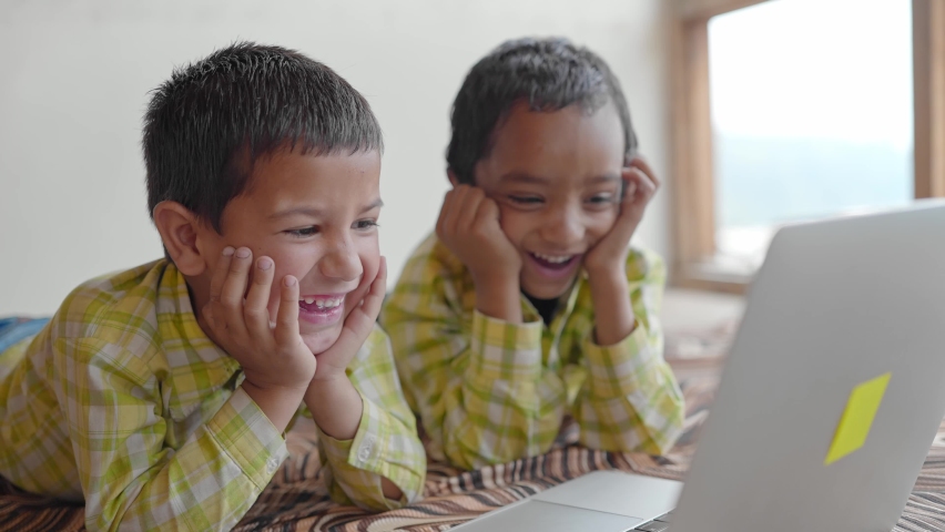 A shot of two Indian Asian preschool or primary male children or kids wearing uniforms is watching a funny video on a laptop and laughing together in an indoor setup. learning and education concept Royalty-Free Stock Footage #1080975701