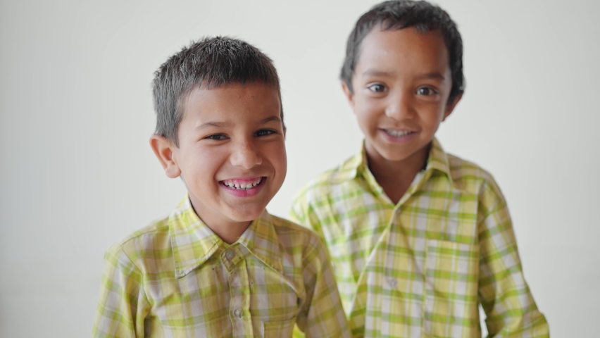 Close shot of two little adorable primary school children wearing uniforms with smiles on their faces staring at the camera standing against a white background or wall. learning and education concept | Shutterstock HD Video #1080975710